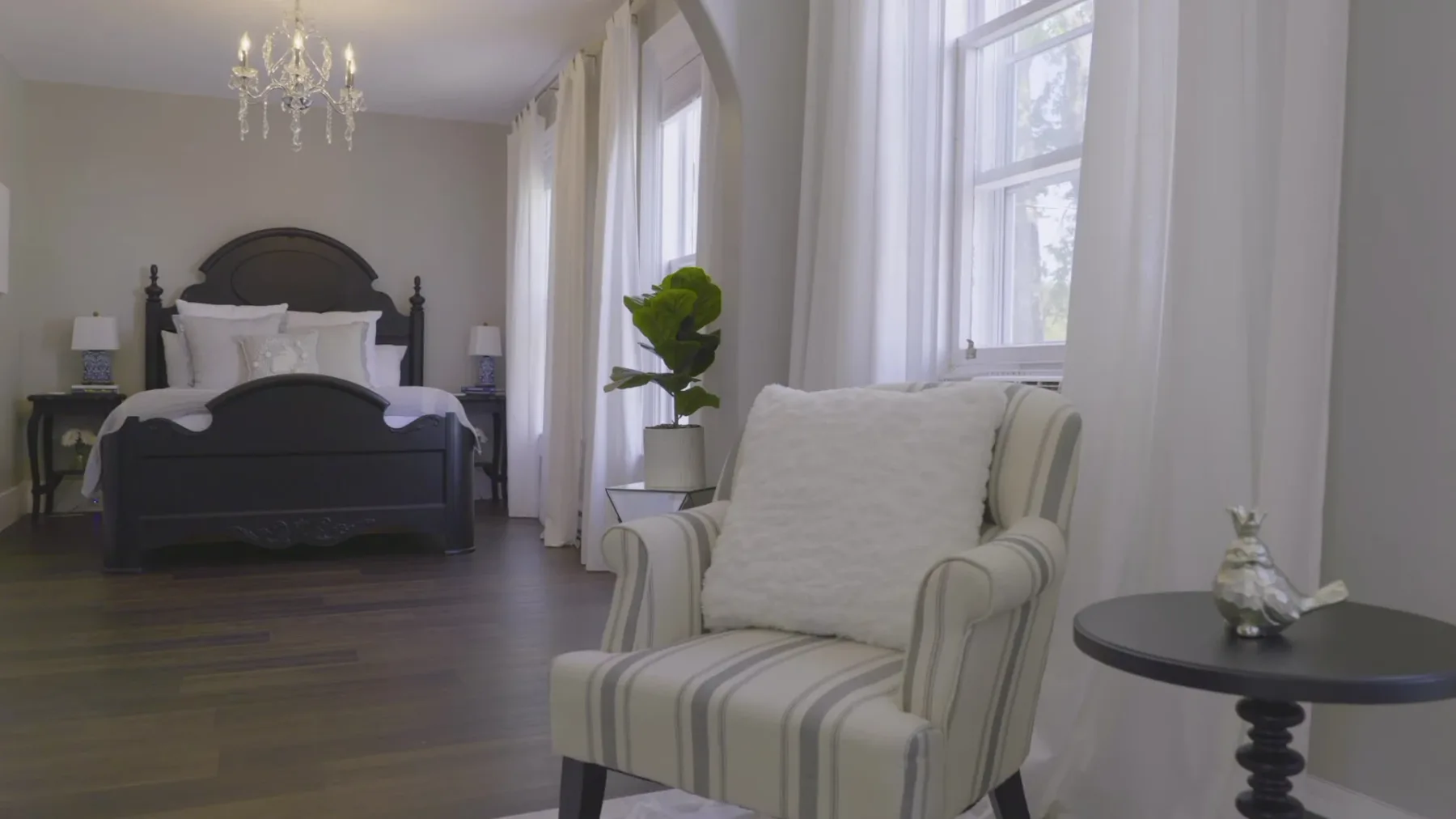 Representative hotel space: A bedroom with a bed and a striped armchair beside tall windows.