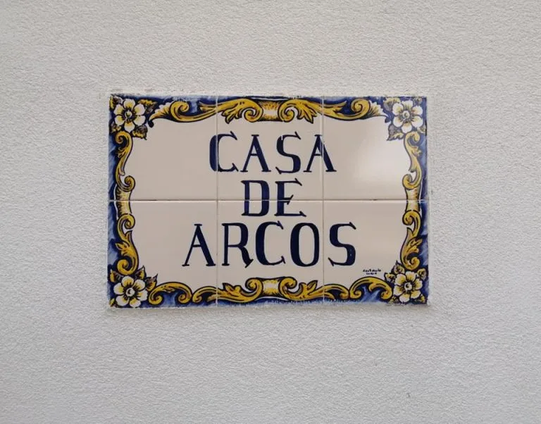 Espacio representativo del hotel: Un letrero decorativo de cerámica que dice «Casa de Arcos» cuelga en una pared blanca.