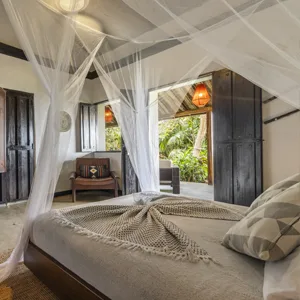 Espacio representativo del hotel: Un dormitorio con una cama con dosel junto a puertas abiertas con vista a la vegetación.
