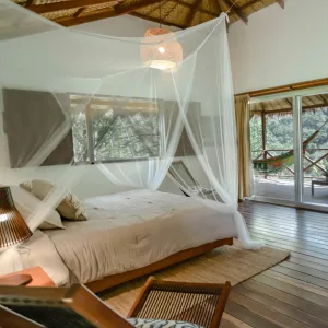 Espacio representativo del hotel: Un dormitorio con una cama cubierta por un dosel y grandes ventanas con vista a los árboles.