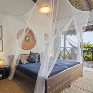 Espacio representativo del hotel: Un dormitorio con una cama cubierta de tela blanca translúcida junto a grandes ventanas.