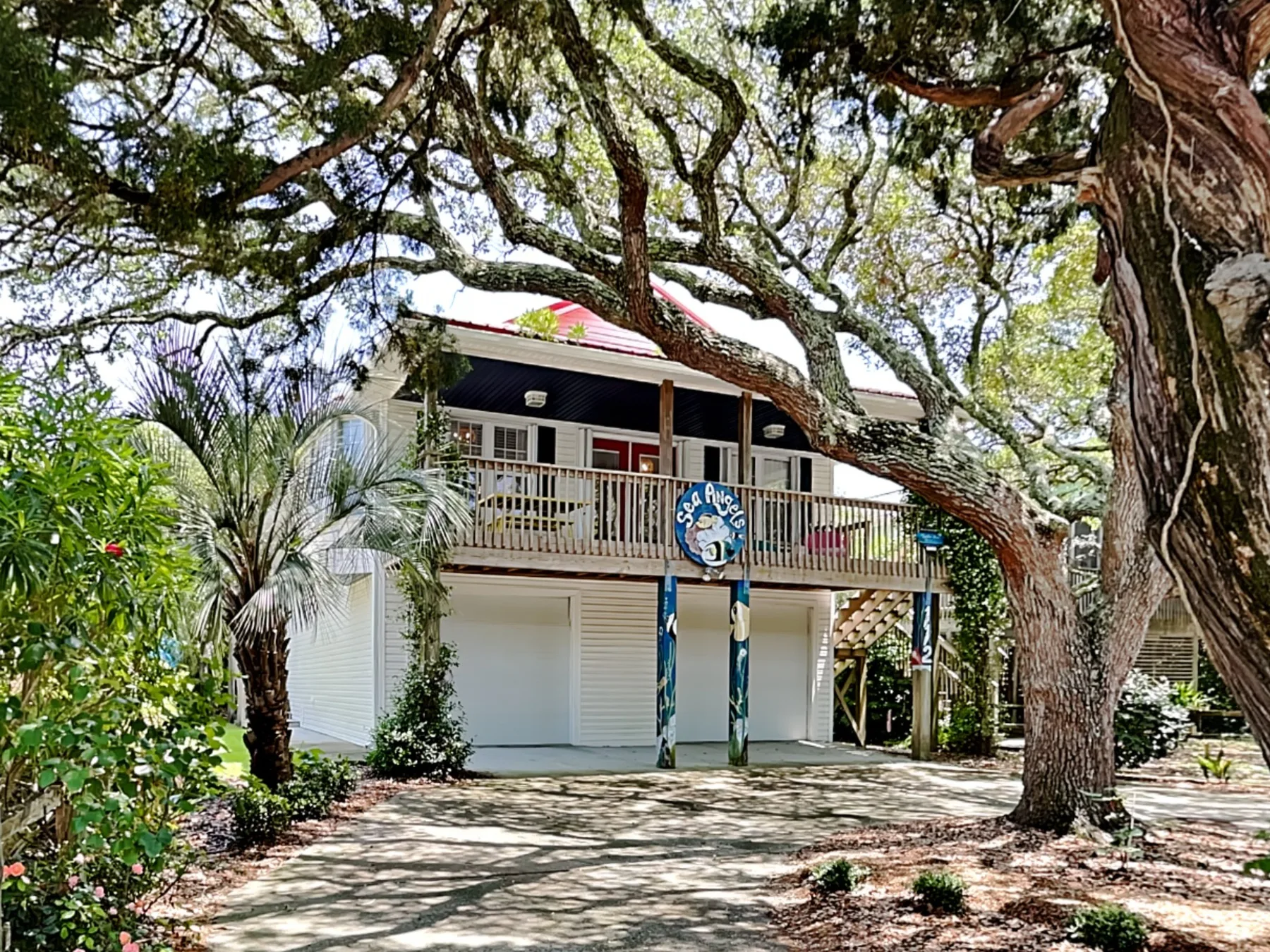 A raised building stands beneath large trees, with a wooden balcony across the front.