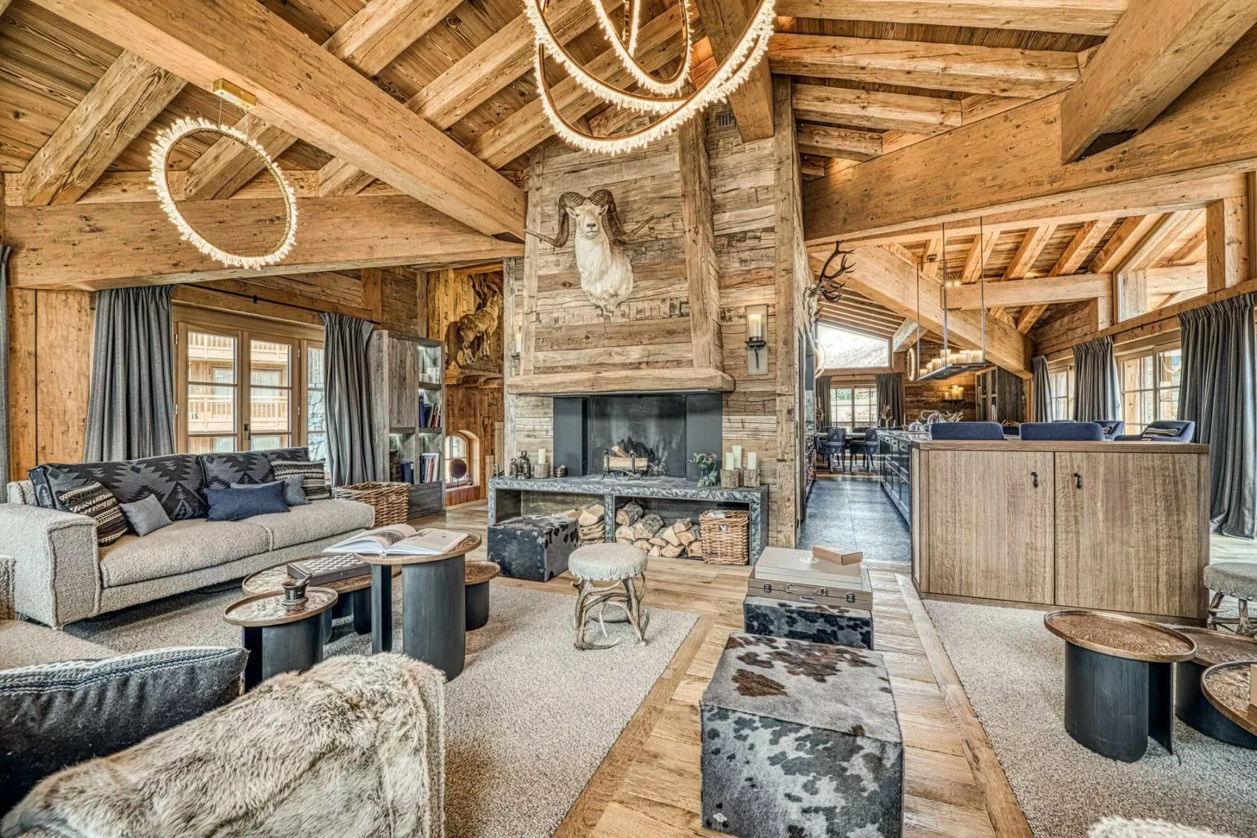 A spacious wood-beamed living room with seating arranged around a stone fireplace.
