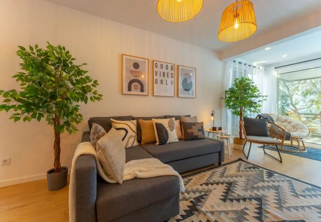 A bright living room with seating, framed wall art, and large windows.
