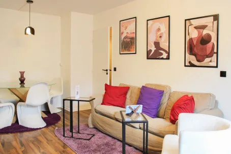 Una sala de estar con cuadros coloridos sobre un sofá y un pequeño comedor.
