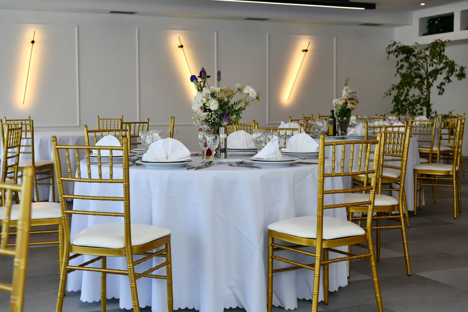 Representative hotel space: A banquet room has round tables set with white linens and gold chairs.