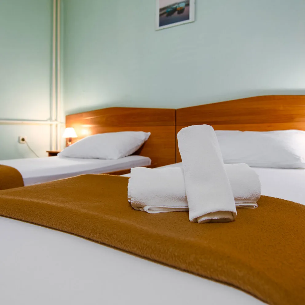 Representative hotel space: A hotel bedroom with two beds and folded towels on the foreground bed.