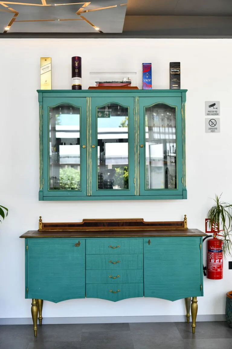 Representative hotel space: A teal cabinet and matching sideboard stand against a white wall.
