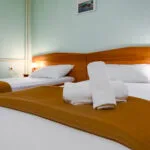 Representative hotel space: A bedroom with a bed dressed in white linens and a brown runner.
