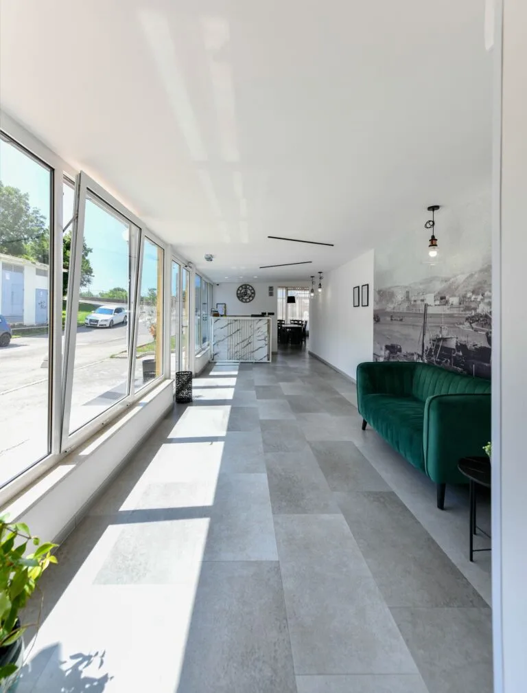 Representative hotel space: A bright lounge with large windows, gray tiled flooring, and green seating.