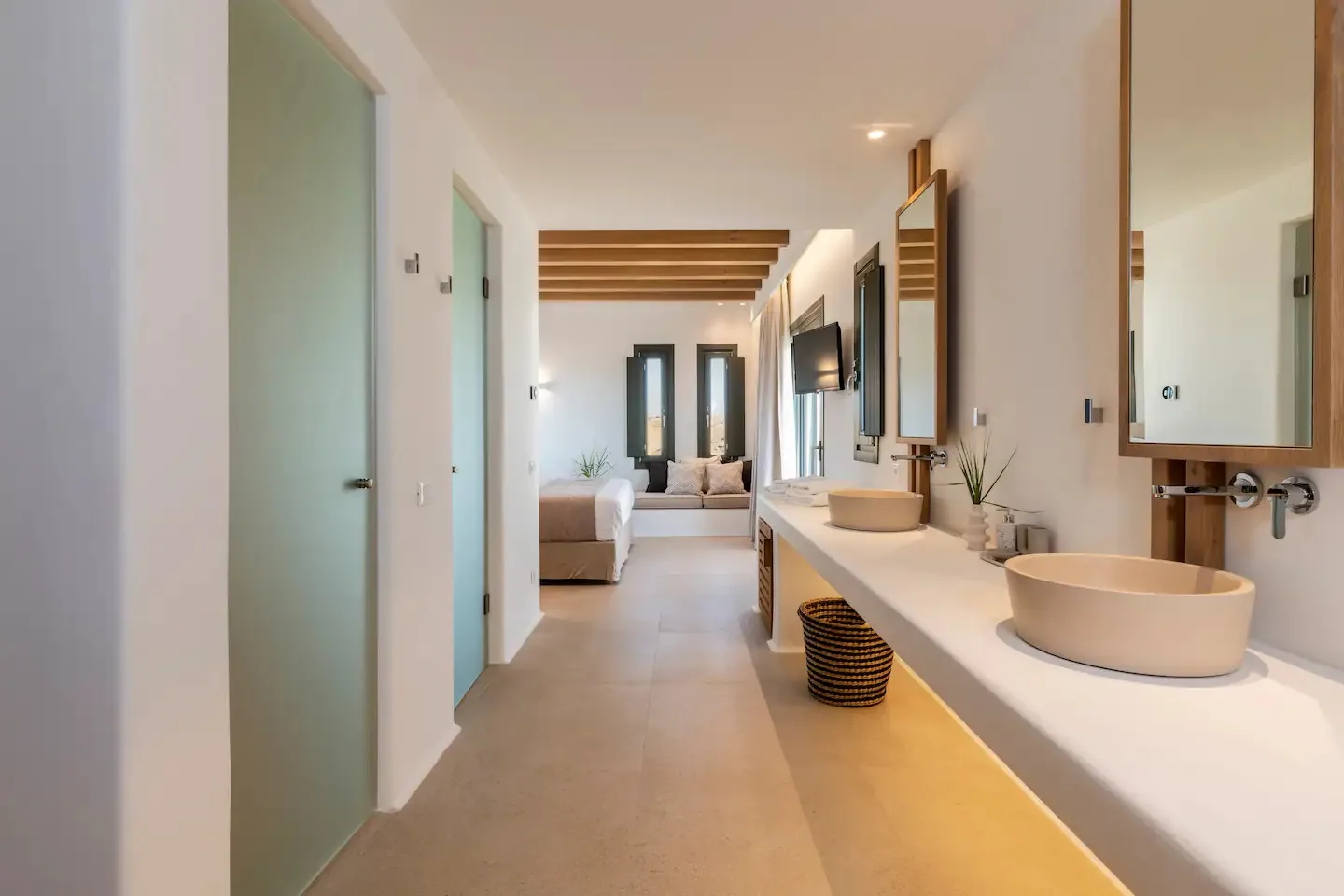 Un tocador de baño con dos lavabos sobrepuestos da a una zona de descanso abierta.