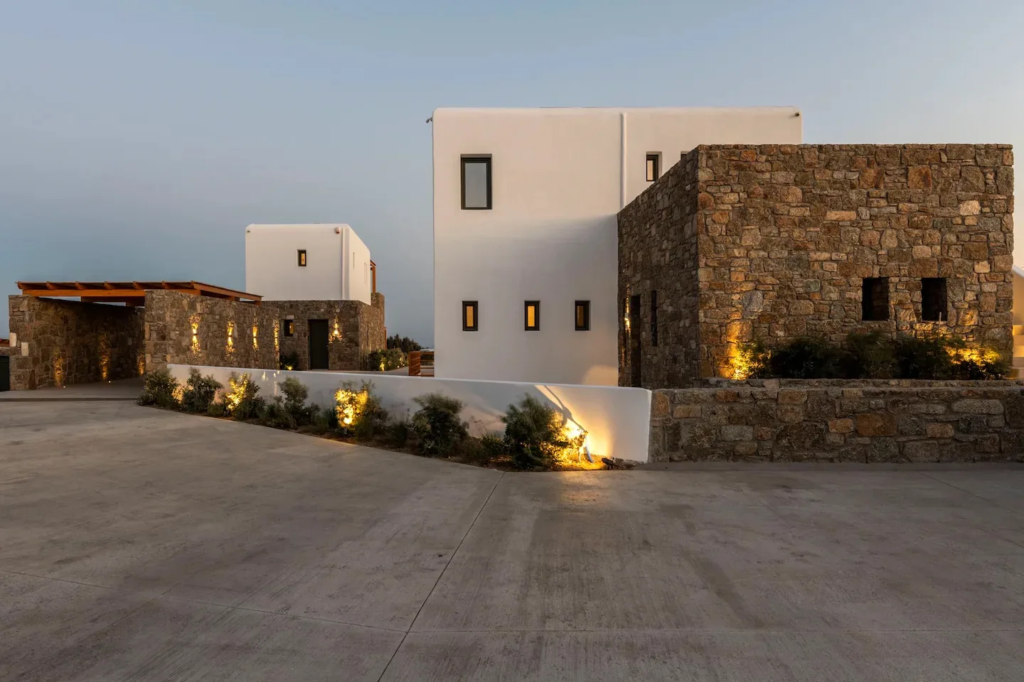 Un edificio moderno con paredes blancas y fachadas de piedra junto a un amplio patio pavimentado.