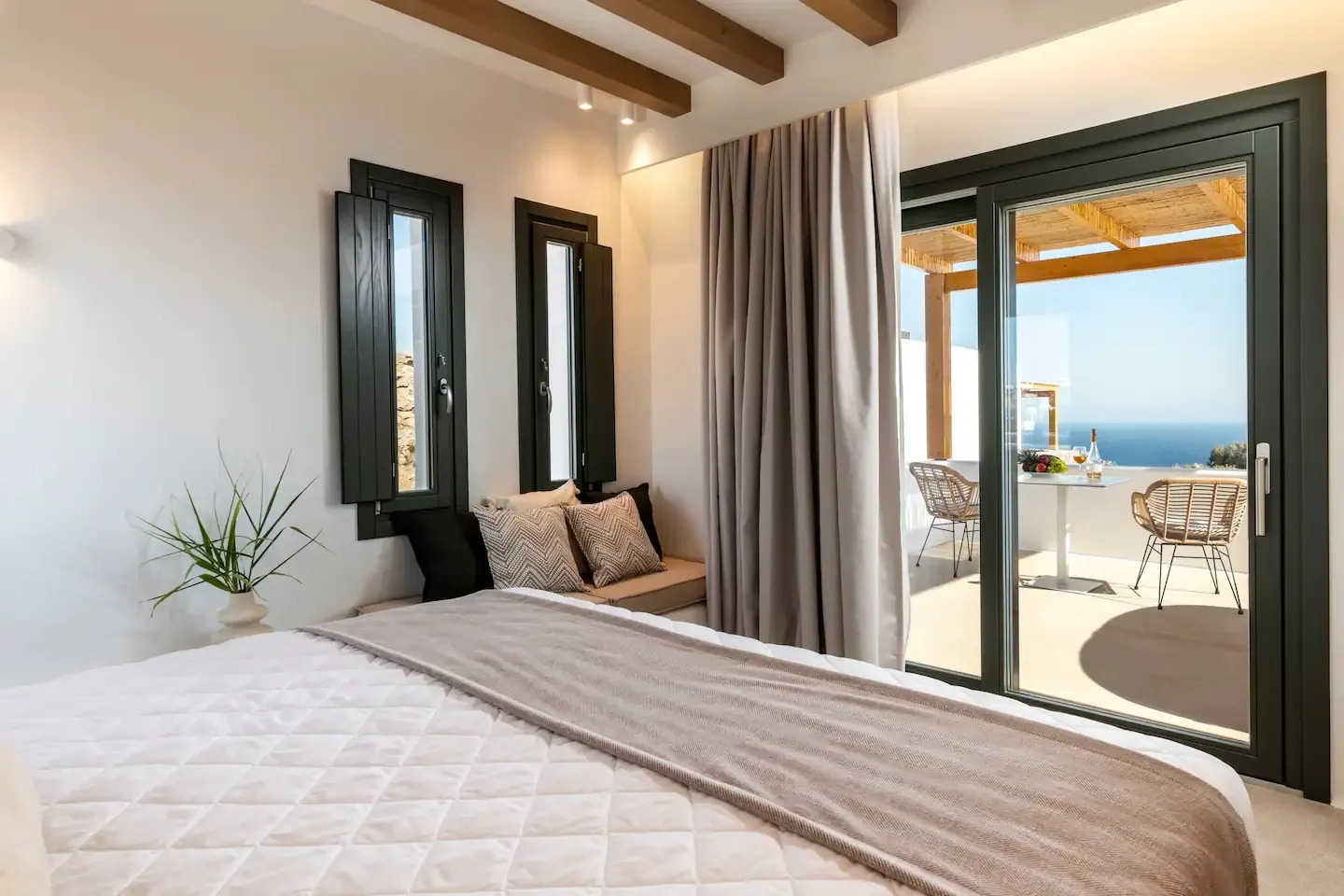 Un dormitorio con una cama junto a puertas de vidrio que dan a una terraza con vistas al mar.