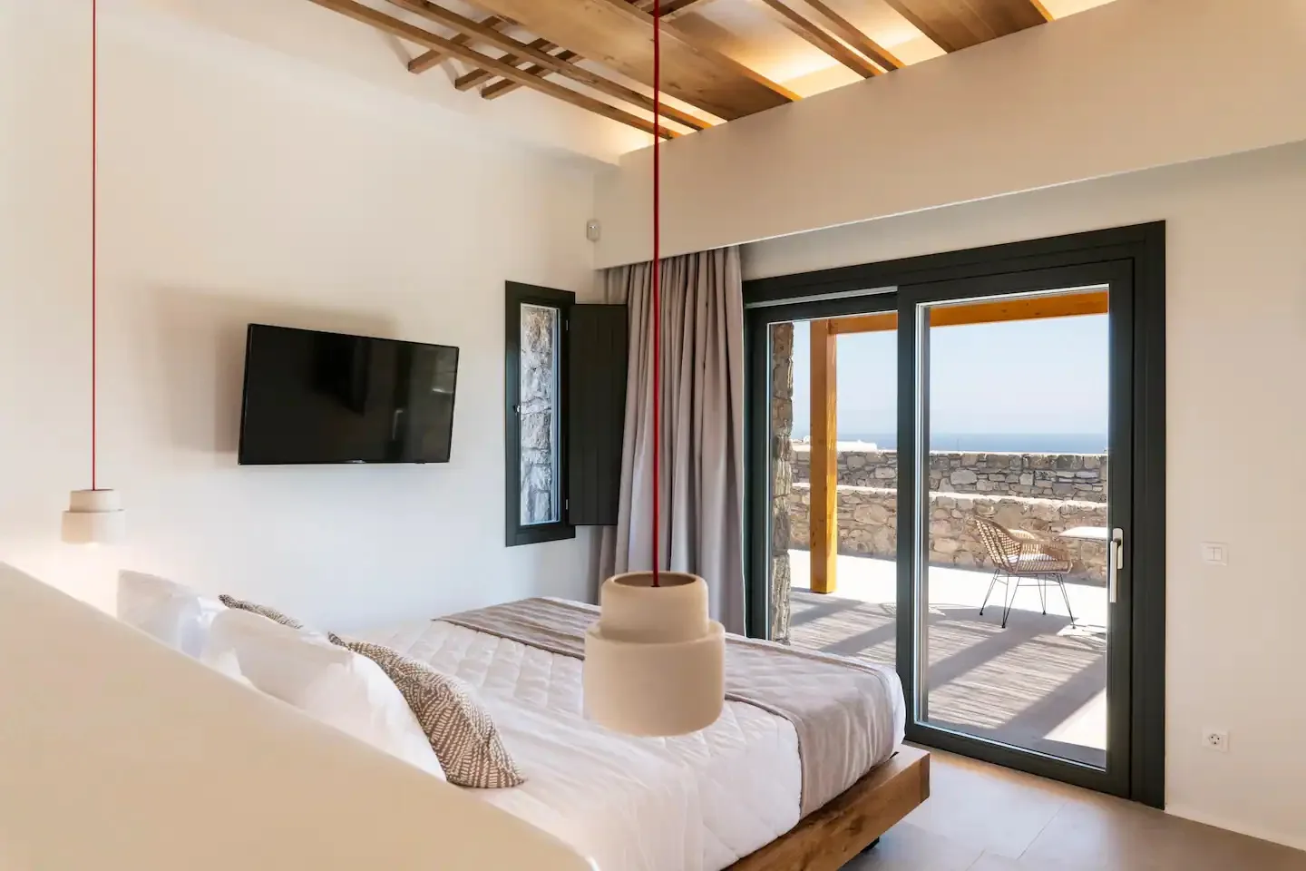 Un dormitorio con una cama, un televisor en la pared y puertas de cristal a una terraza.
