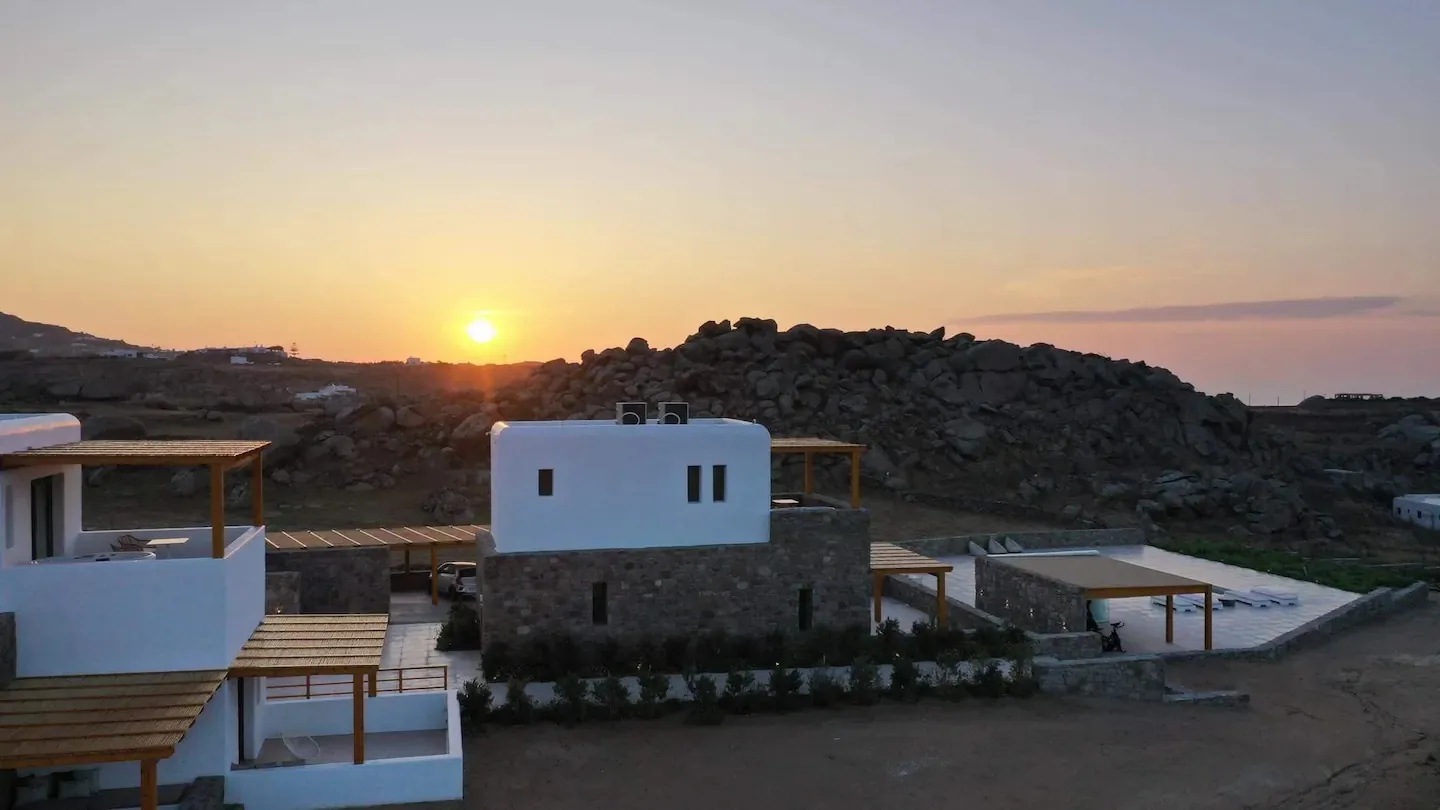Edificios blancos se encuentran entre colinas rocosas bajo el sol poniente.