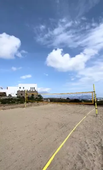 Una cancha exterior de arena con una red bajo un cielo parcialmente nublado.