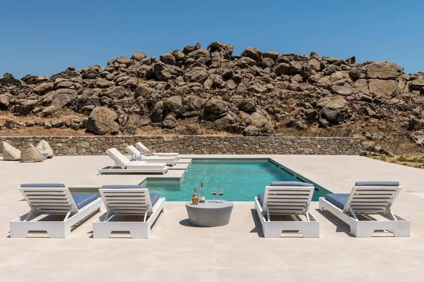 Una piscina al aire libre está rodeada de tumbonas y terreno rocoso.