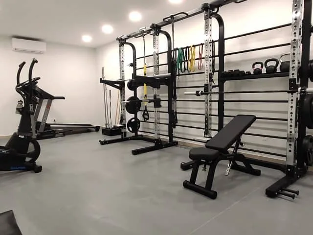 Un gimnasio con soportes de pesas, equipo de ejercicio y un banco de entrenamiento.