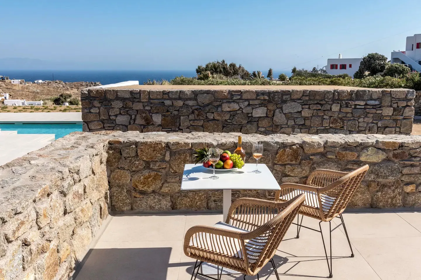Patio exterior con asientos de mimbre, una mesa con fruta y vistas al mar.