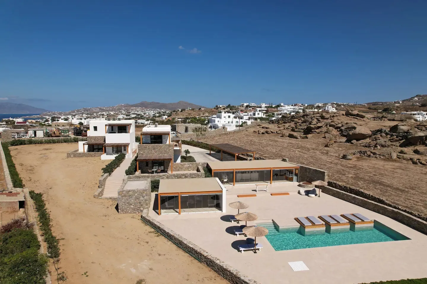 Un conjunto de villas modernas con piscina se encuentra en un paisaje seco y rocoso.