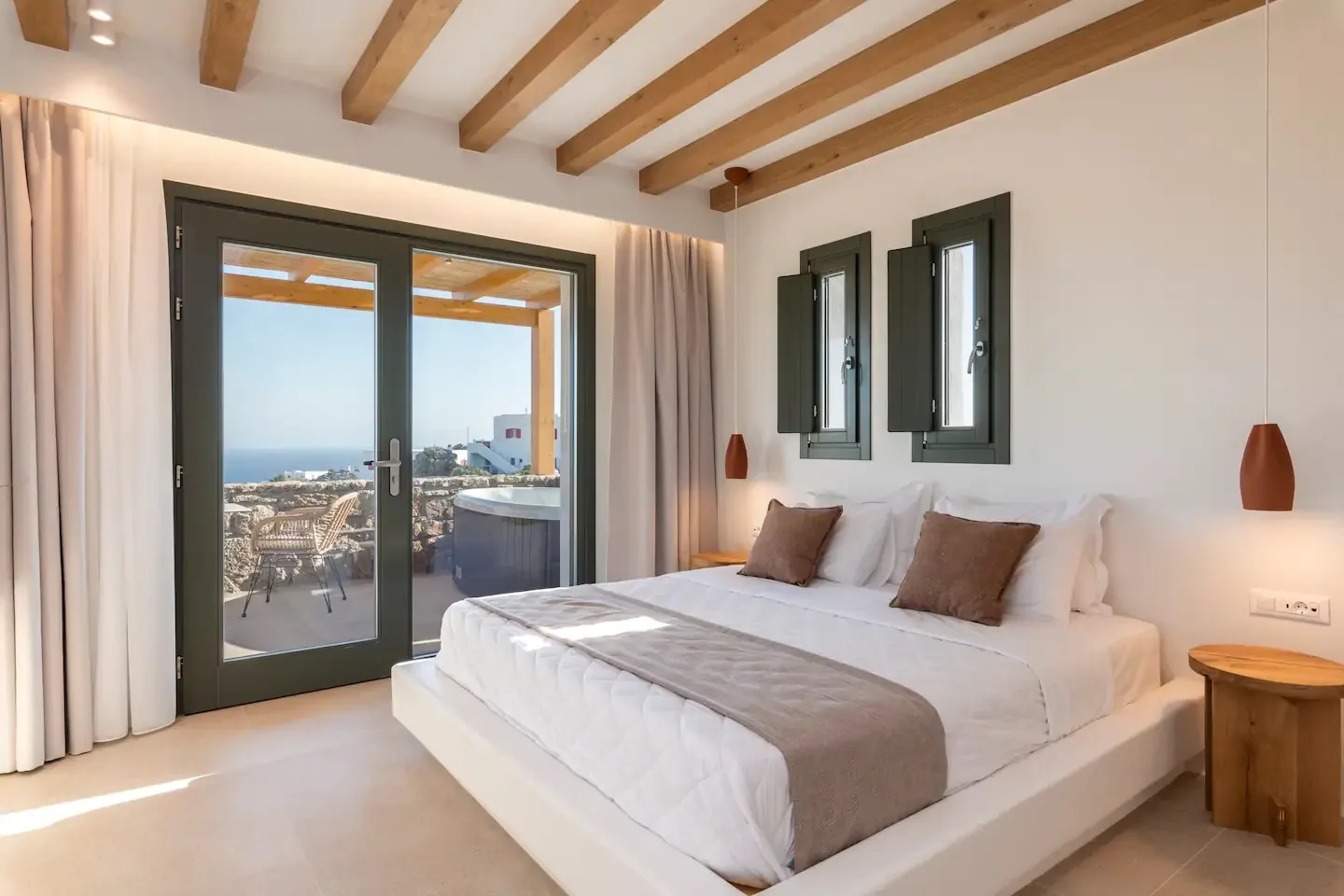 Un dormitorio con una cama grande, vigas vistas y puertas de cristal que dan a un balcón.