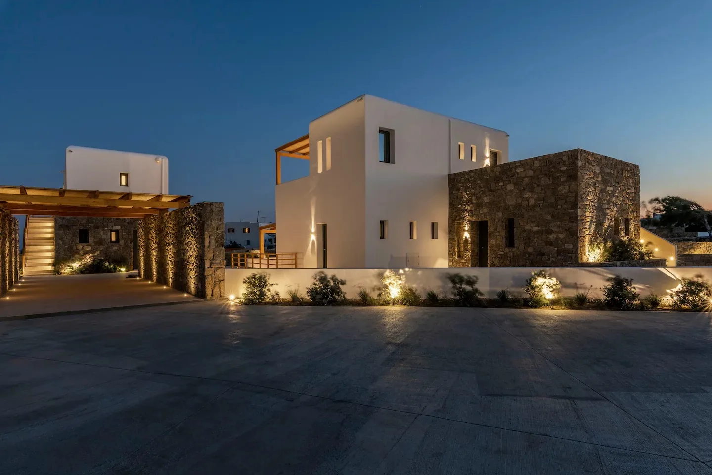 Un edificio moderno con paredes blancas y secciones de piedra está iluminado al anochecer.