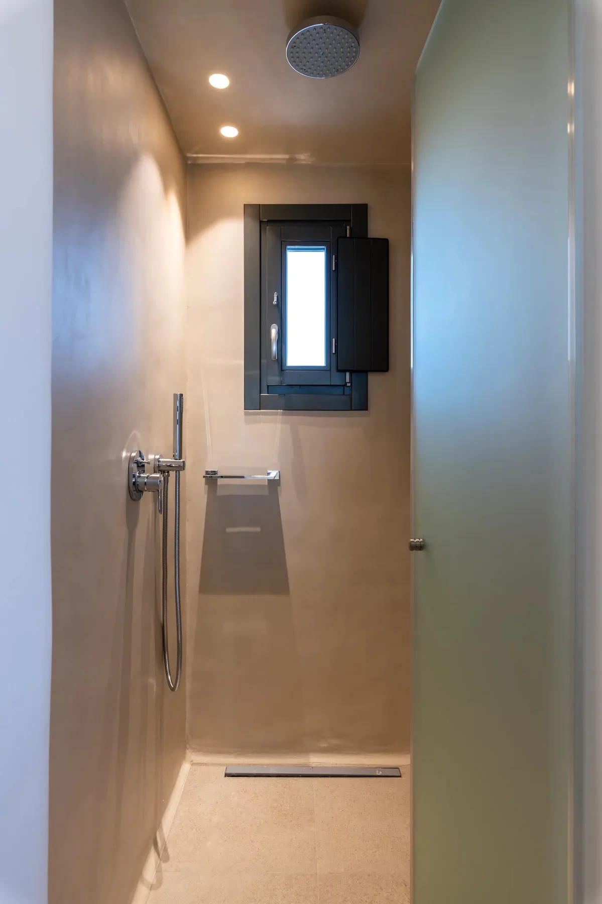 Una ducha a ras de suelo con cabezal montado en la pared y una ventana estrecha.