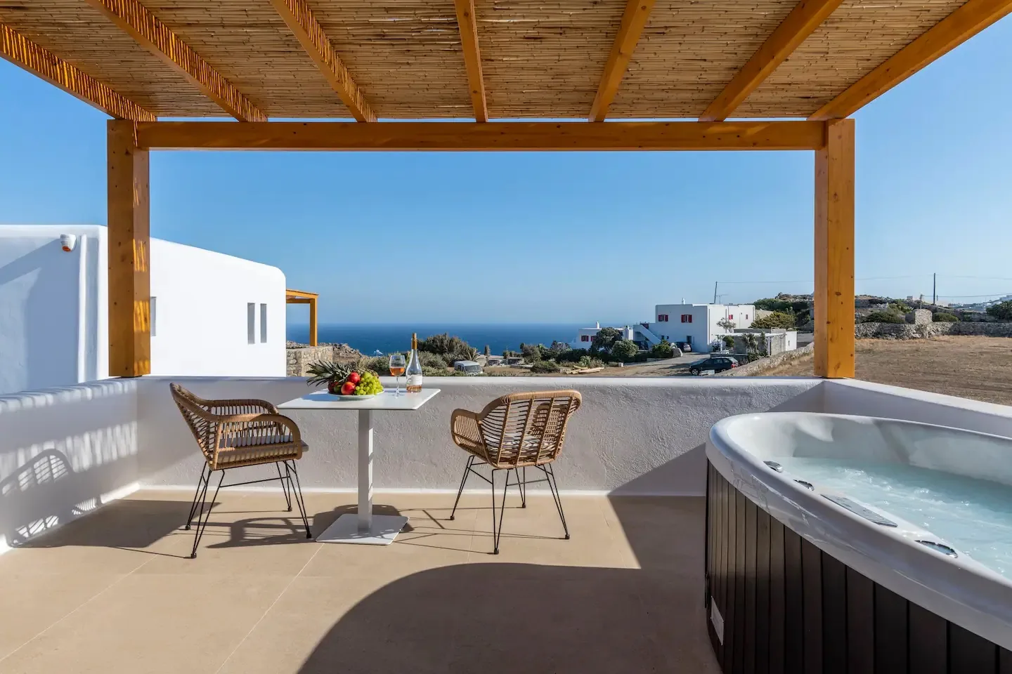 Un patio cubierto tiene una mesa pequeña y asientos junto a un jacuzzi, con vistas al mar.