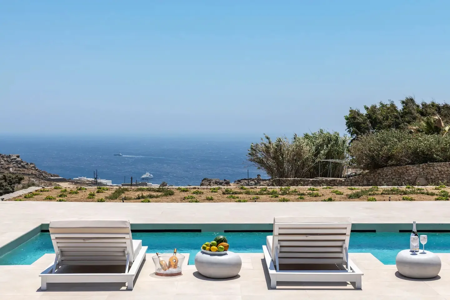 Una terraza junto a la piscina mira al mar, con tumbonas junto al agua.