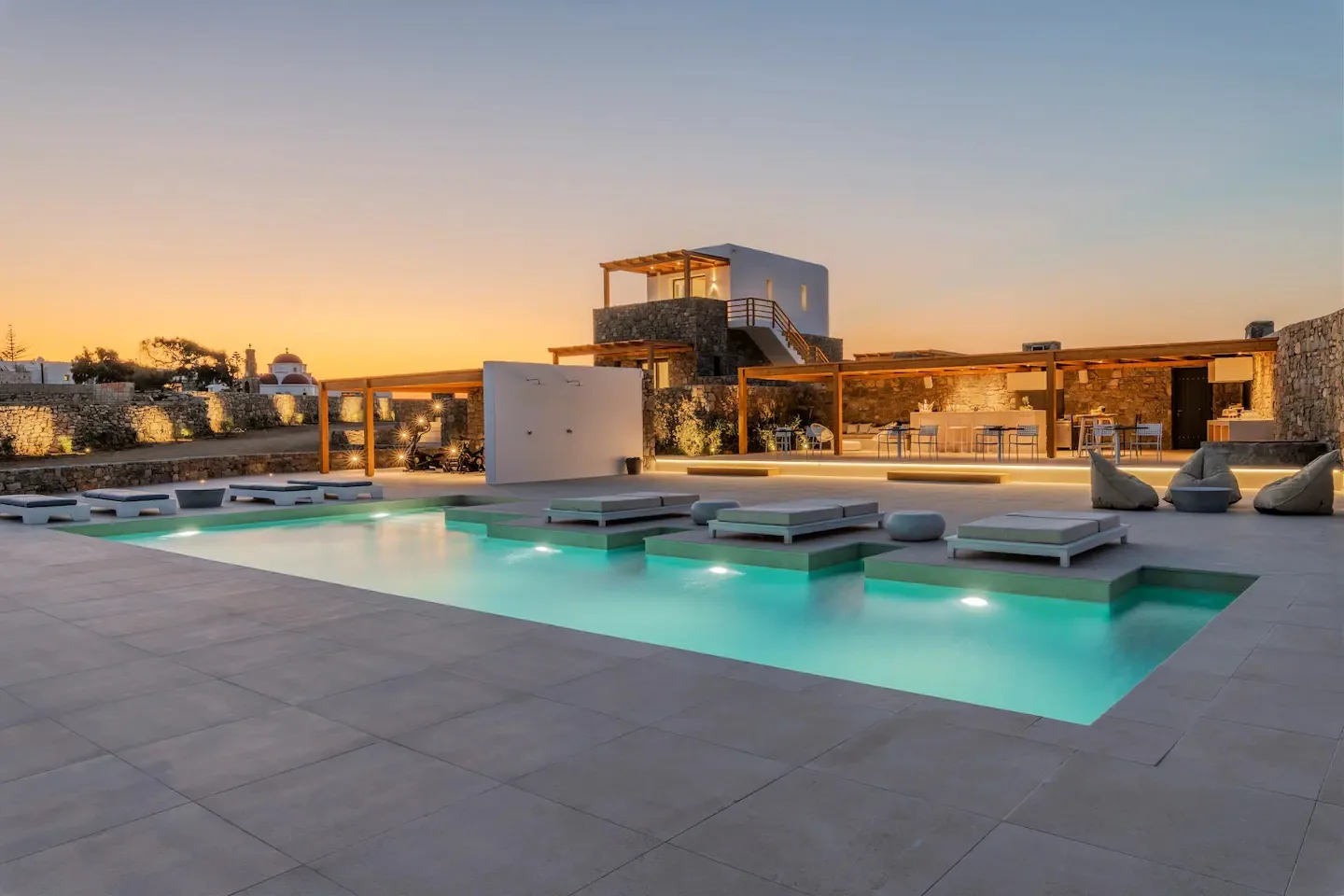 Una piscina exterior iluminada junto a un edificio moderno al atardecer.