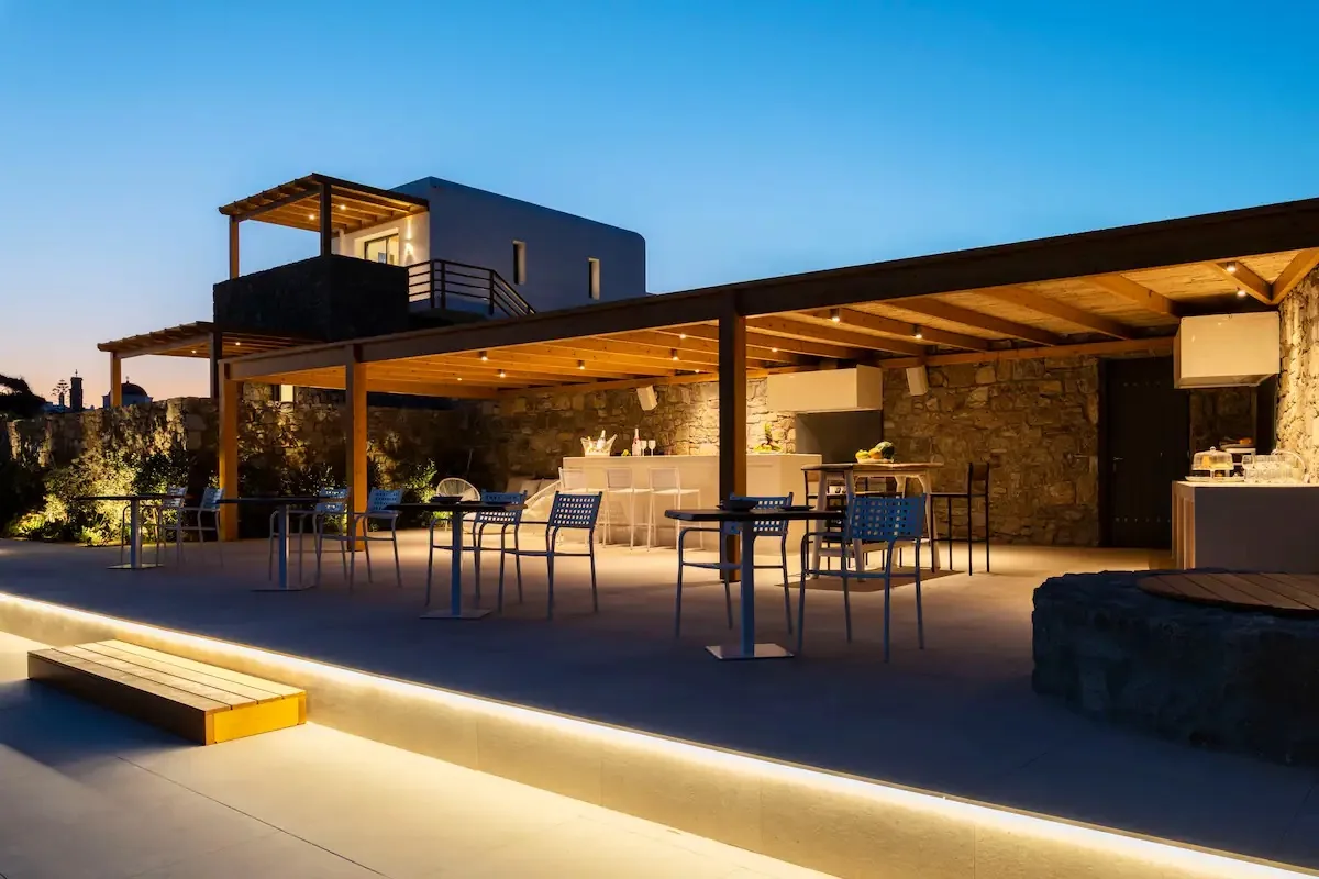 Una zona de comedor exterior bajo un patio cubierto, con mesas y sillas.