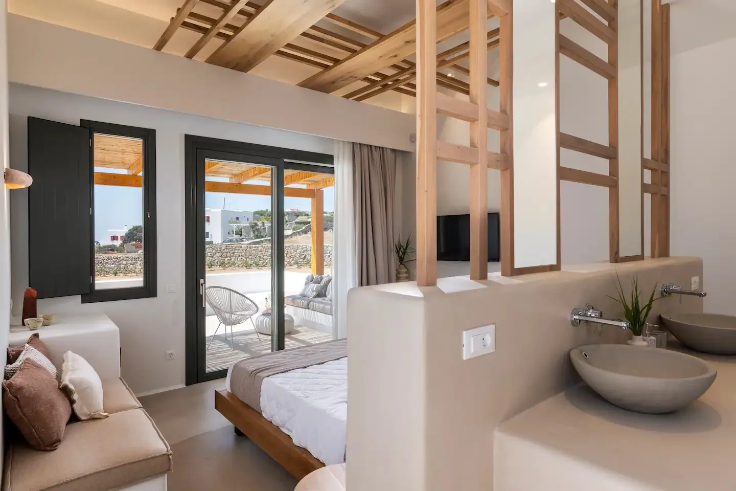 Un dormitorio moderno con cama, zona de estar y puertas corredizas de vidrio que dan a un patio.