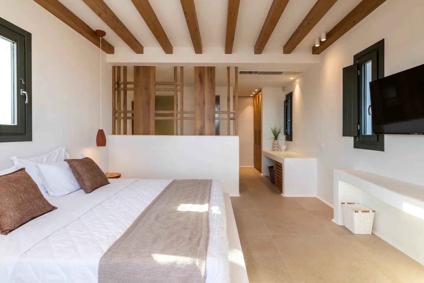 Un dormitorio luminoso con una cama, vigas expuestas en el techo y un televisor en la pared.