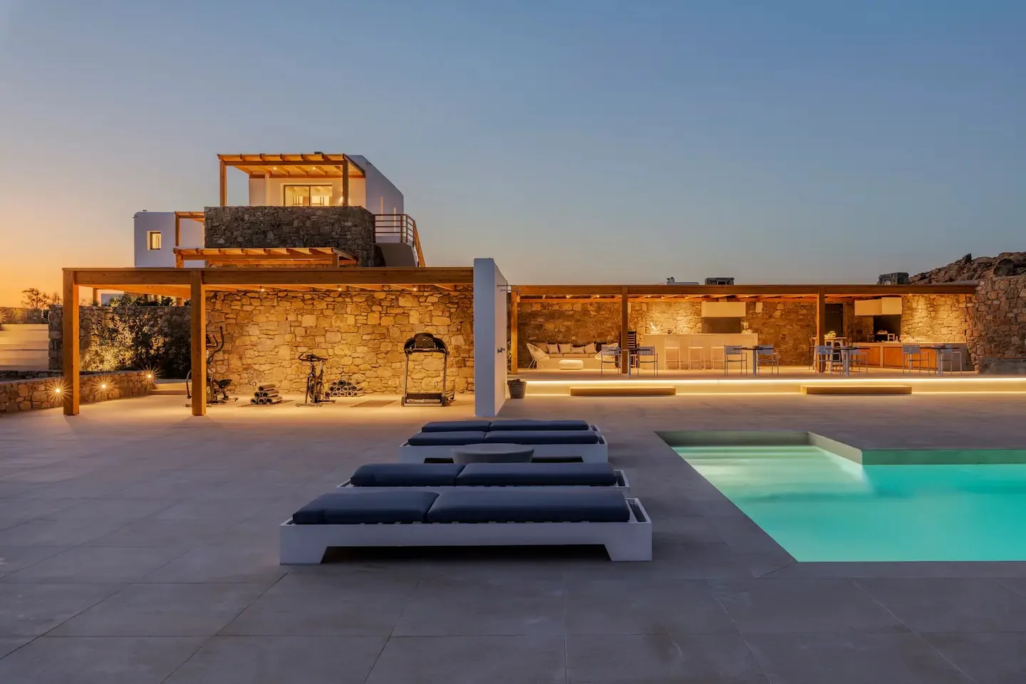 Una zona de piscina al aire libre con asientos y un edificio iluminado al anochecer.