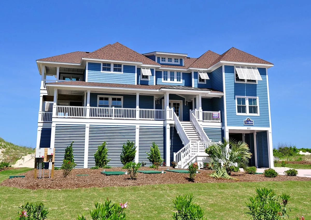 Una gran casa azul de estilo costero con amplios porches blancos y escaleras exteriores.