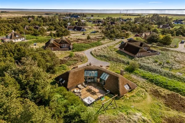 An aerial view of a thatched-roof house surrounded by greenery and winding paths.