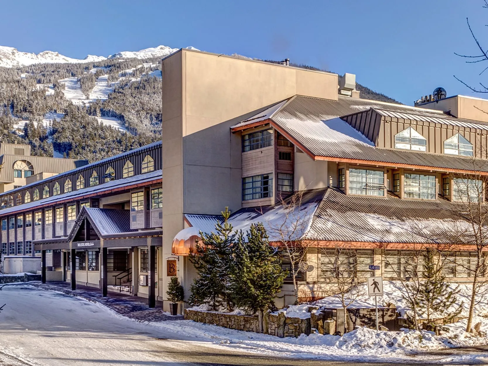 Espacio representativo del hotel: Un edificio grande con techos cubiertos de nieve se alza al pie de una montaña bajo un cielo despejado.