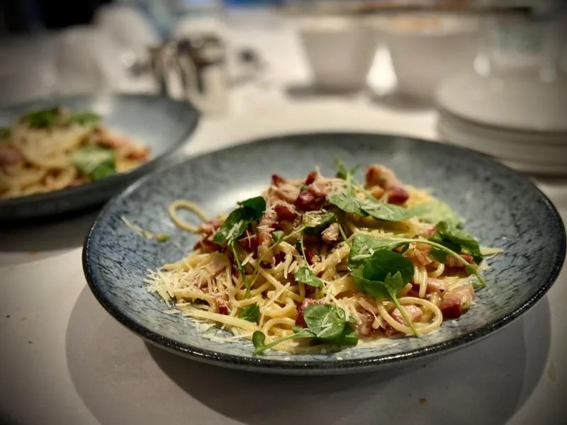 Representative hotel space: A plated pasta dish with greens and grated cheese sits on a dining table.