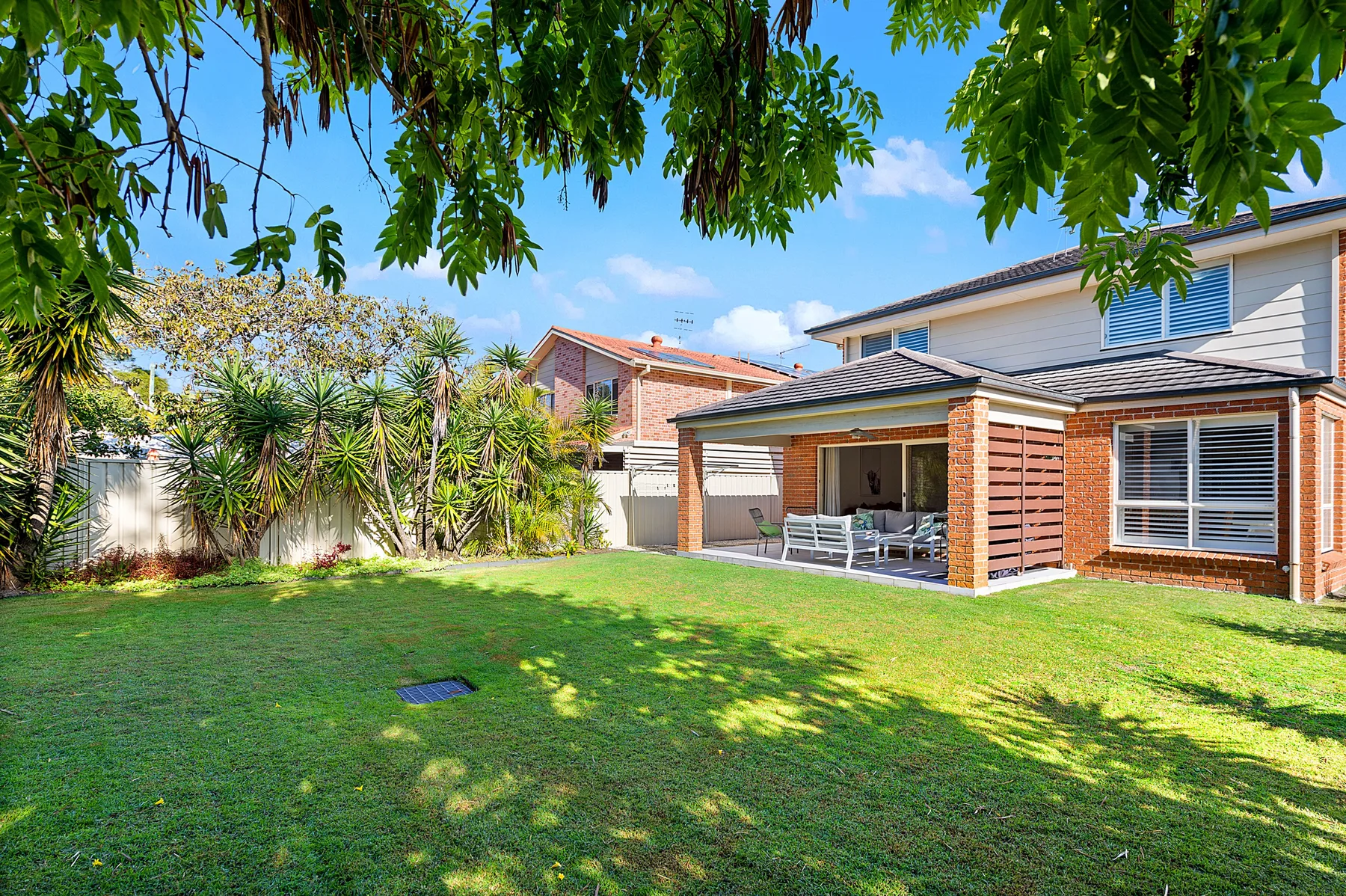 A grassy backyard with a covered patio beside a brick house.