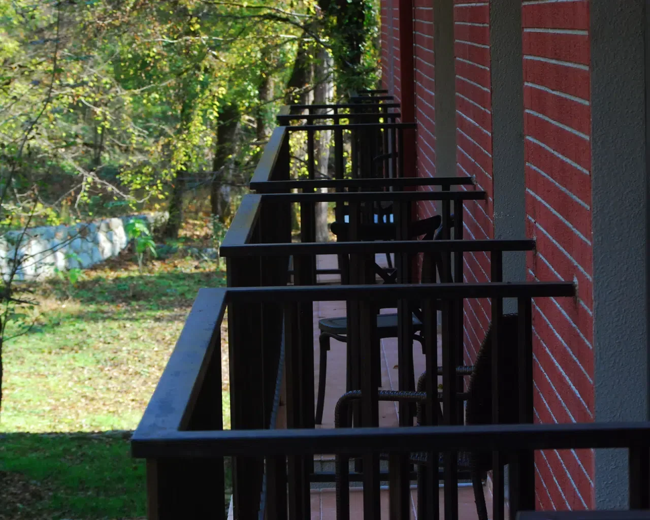 Espacio representativo del hotel: Una fila de pequeños balcones con barandillas negras da a un jardín frondoso.