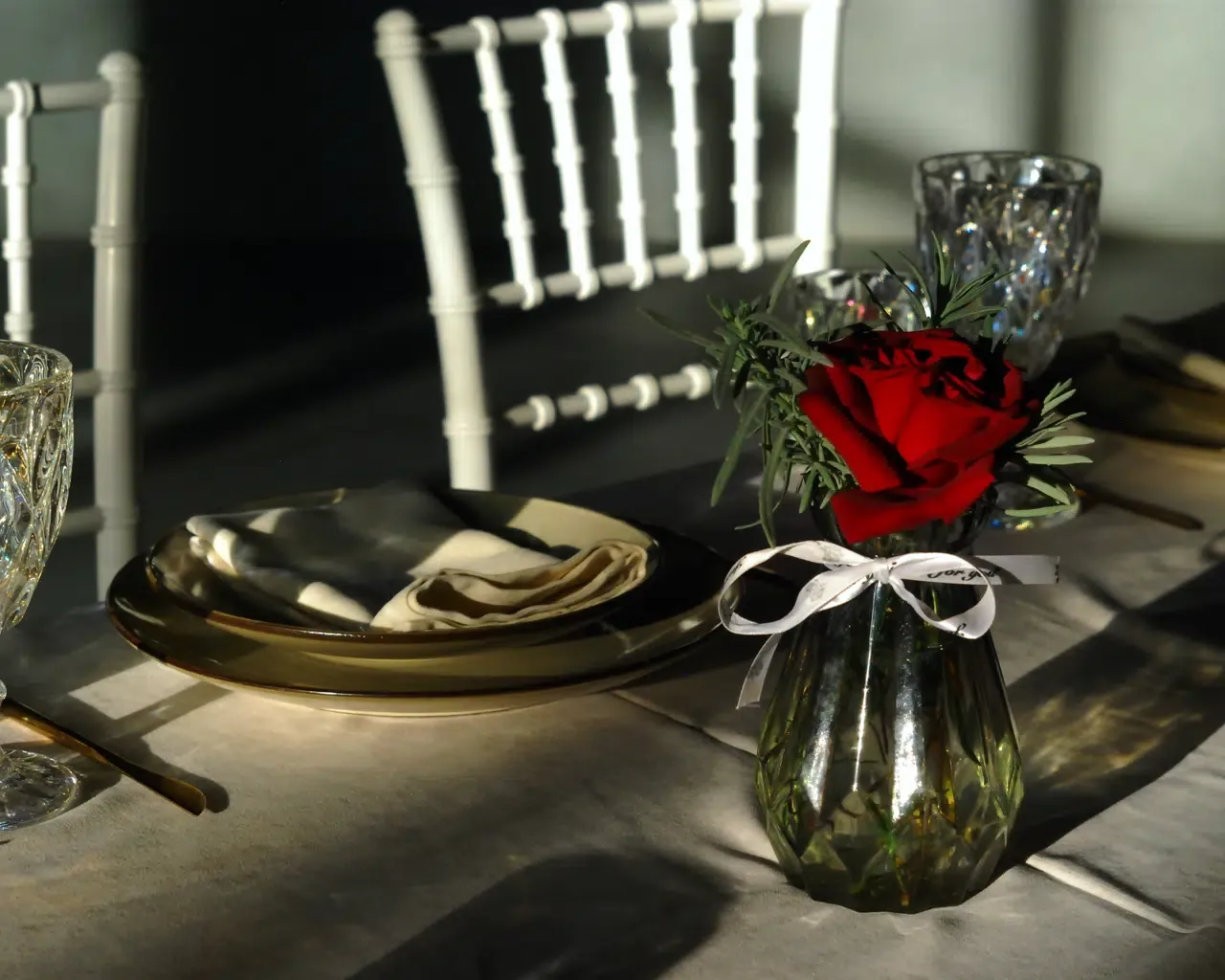 Espacio representativo del hotel: Una mesa de comedor está preparada con platos, servilletas dobladas y una rosa roja.