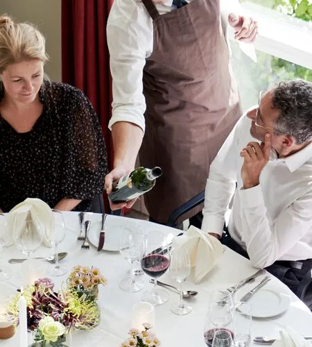Representative hotel space: A server pours wine for diners seated at a set table.