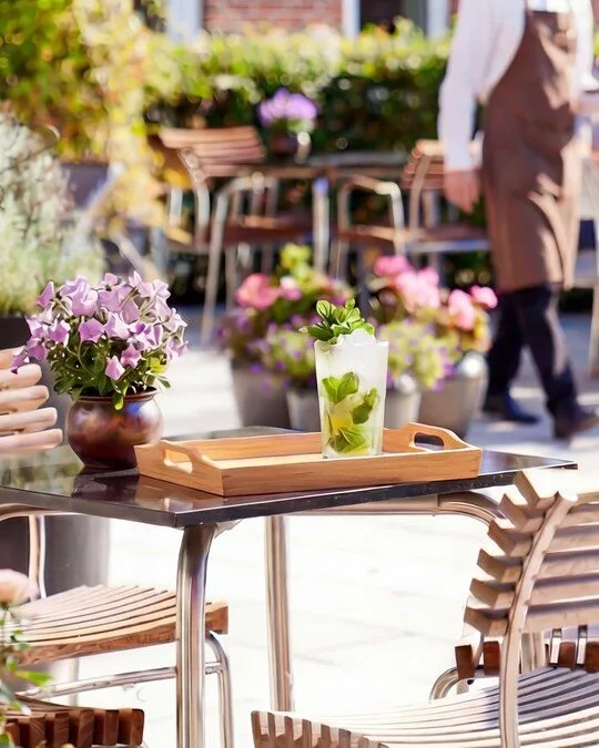 Representative hotel space: A flower-filled outdoor café patio has wooden seating and a table with a drink.