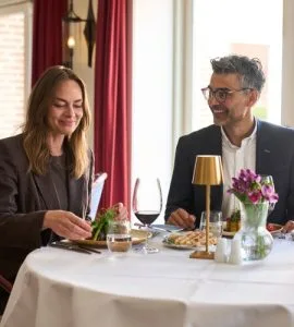 Representative hotel space: A dining table set with flowers and glassware beside two seated people.