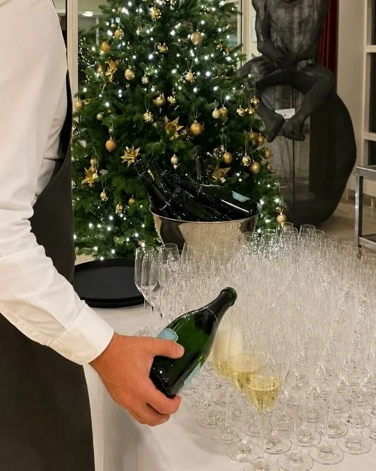 Representative hotel space: A person pours sparkling wine beside a decorated Christmas tree and rows of glasses.