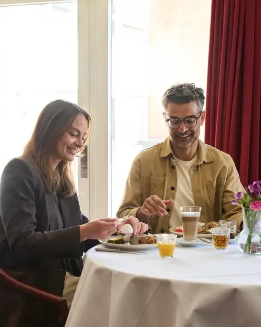 Representative hotel space: A couple shares breakfast at a table beside a bright window.