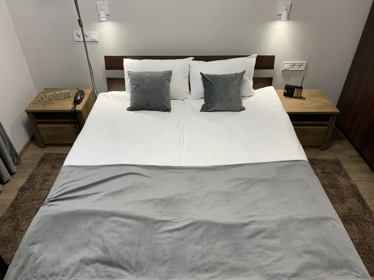 Espacio representativo del hotel: Una cama de dormitorio bien tendida, con ropa de cama blanca y almohadas grises.