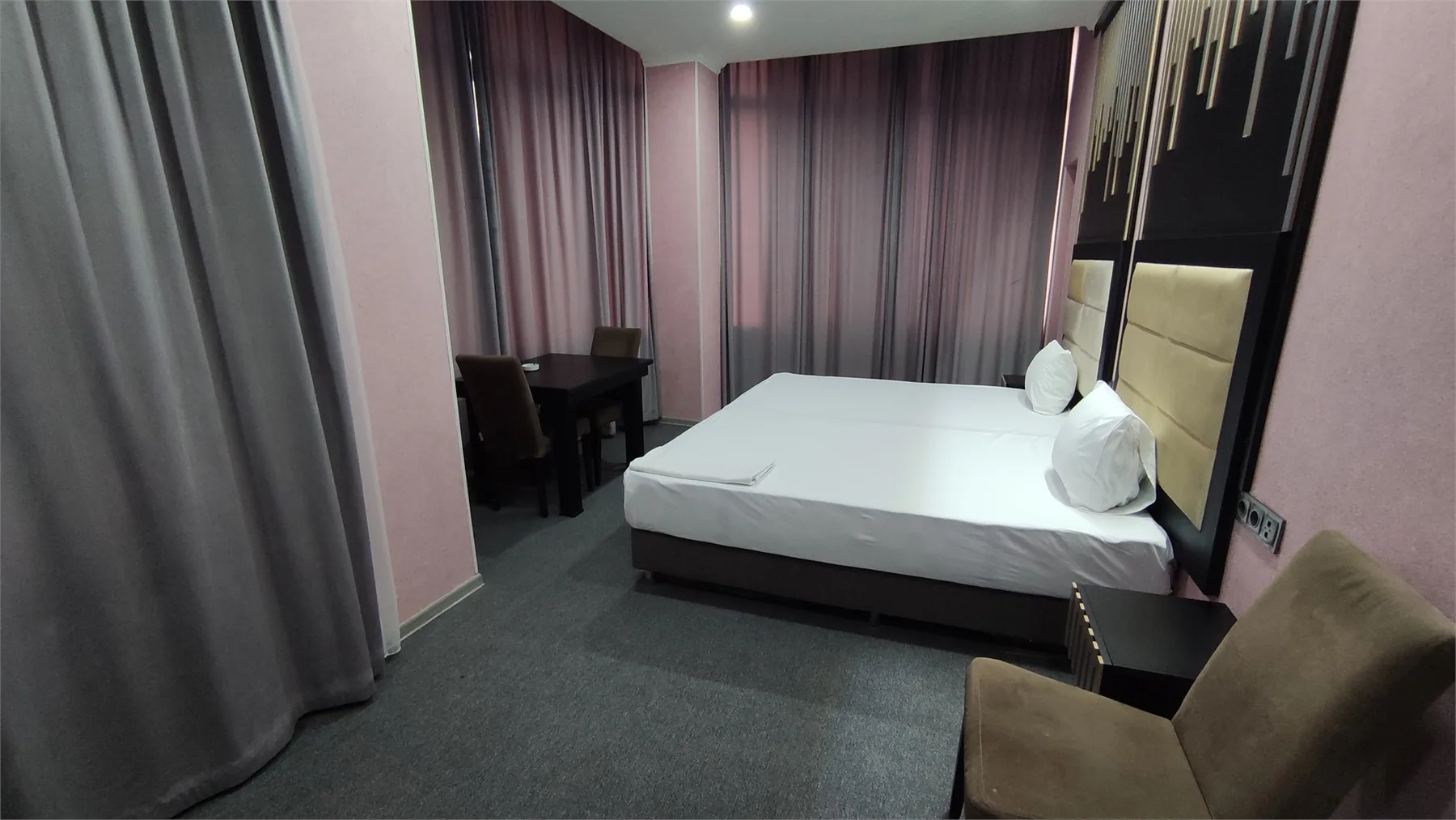 Representative hotel space: A bedroom with a bed, bedside table, and curtains.