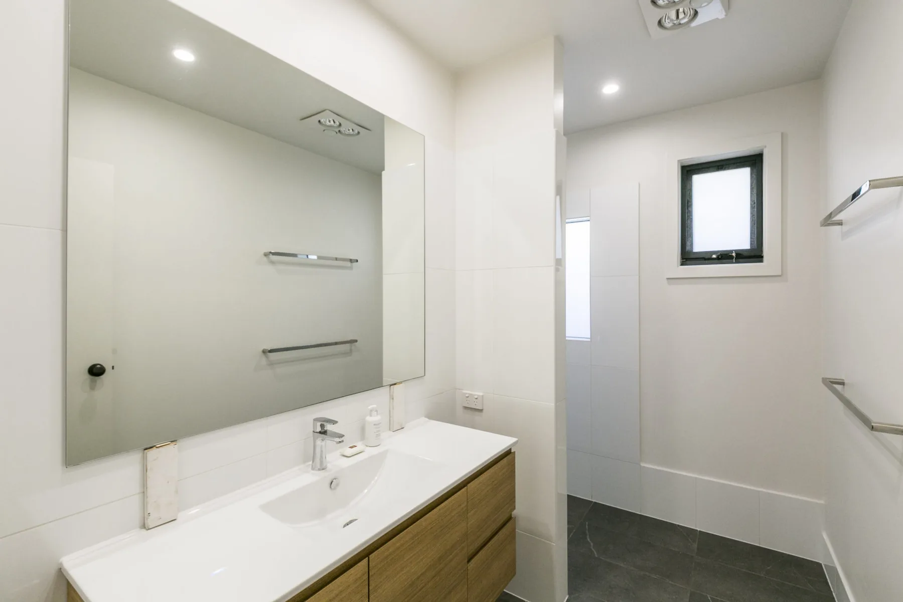 Un baño luminoso con un espejo amplio, lavabo y ducha de vidrio.
