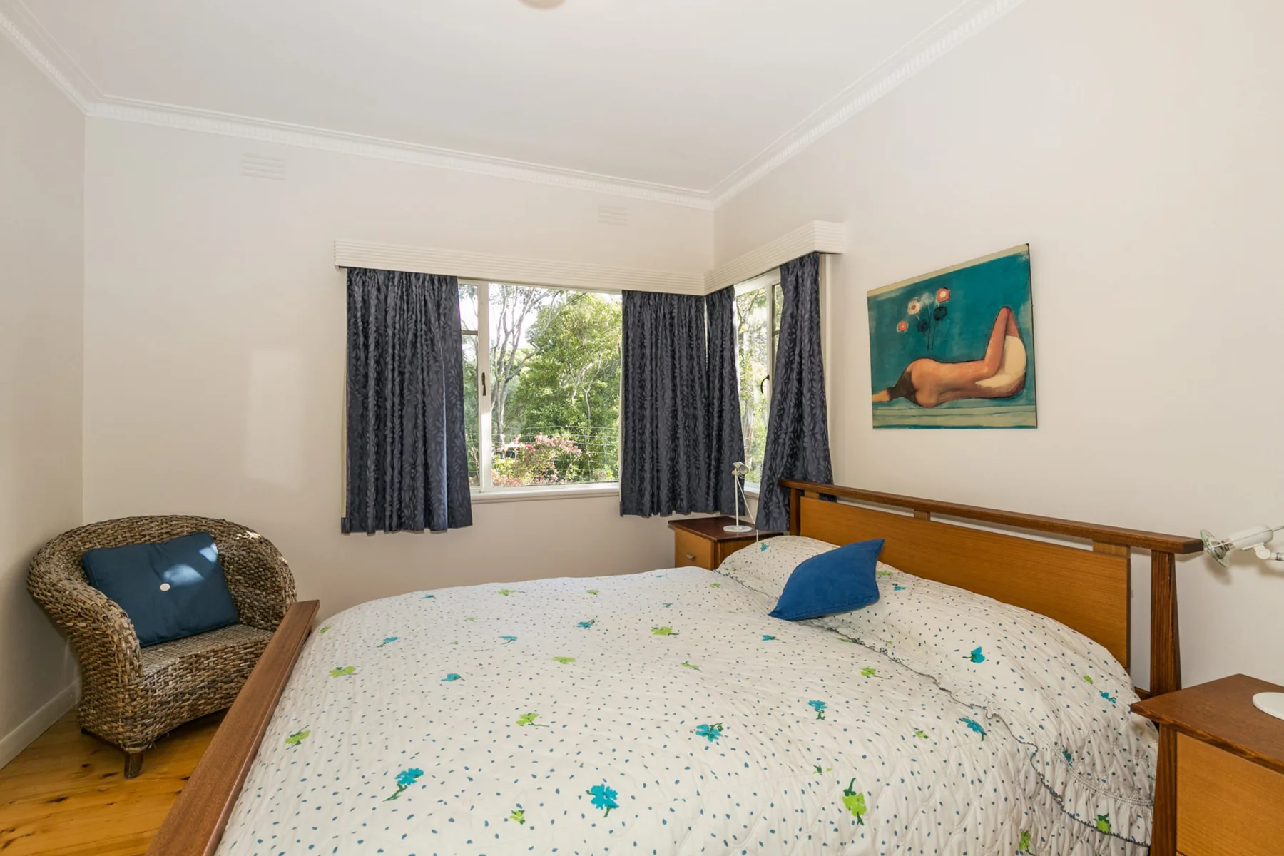 Un dormitorio con una cama, una silla de mimbre y una ventana con cortinas oscuras.